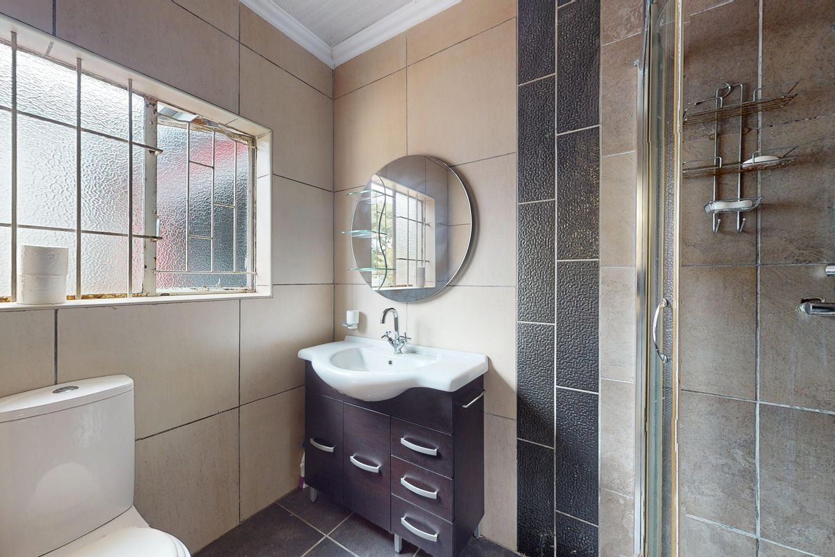 A functional bathroom featuring a vanity basin, a shower enclosure with a mixer, and a toilet, finished with neutral wall and floor tiling.