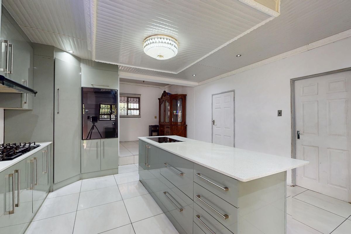 Modern kitchen featuring sleek cabinetry, a central island with a stone countertop, integrated appliances, and bright tiled flooring.