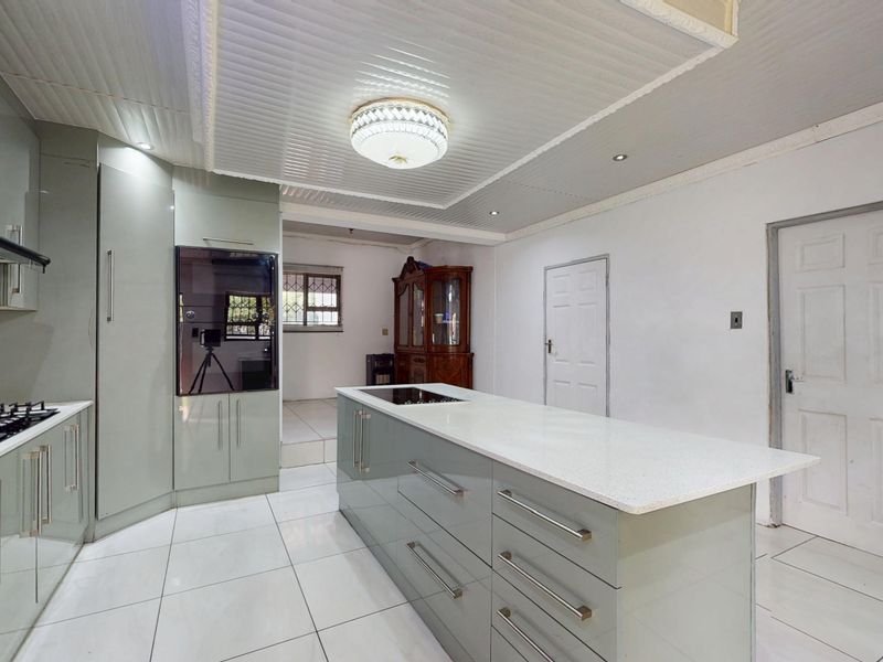 Modern kitchen featuring sleek cabinetry, a central island with a stone countertop, integrated appliances, and bright tiled flooring.