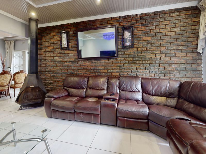 Spacious living area featuring a prominent exposed brick wall, a modern freestanding metal fireplace, and neutral tiled flooring throughout.