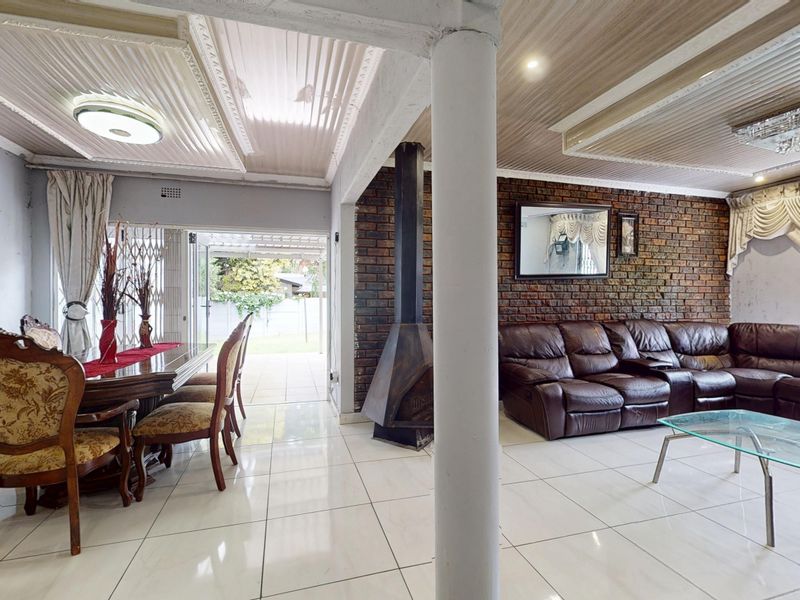 Open-plan living and dining area featuring tiled floors, an exposed brick feature wall, and a central freestanding fireplace.