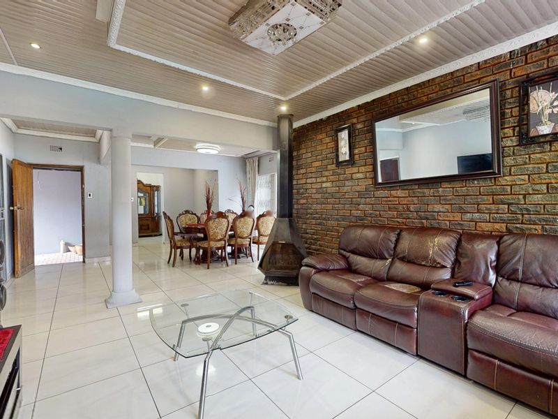Spacious open-plan living and dining area featuring a prominent exposed brick wall, a freestanding fireplace, and neutral tiled flooring throughout.