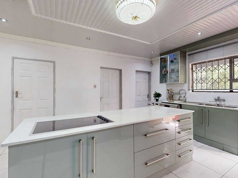 Modern kitchen featuring a central island with an integrated induction hob, quartz countertops, ample cabinetry, and tiled flooring with natural light.