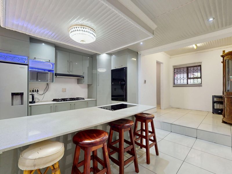Open-plan kitchen featuring modern cabinetry, quartz countertops, a central island with a hob, and tiled flooring, seamlessly flowing into an adjacent living area.