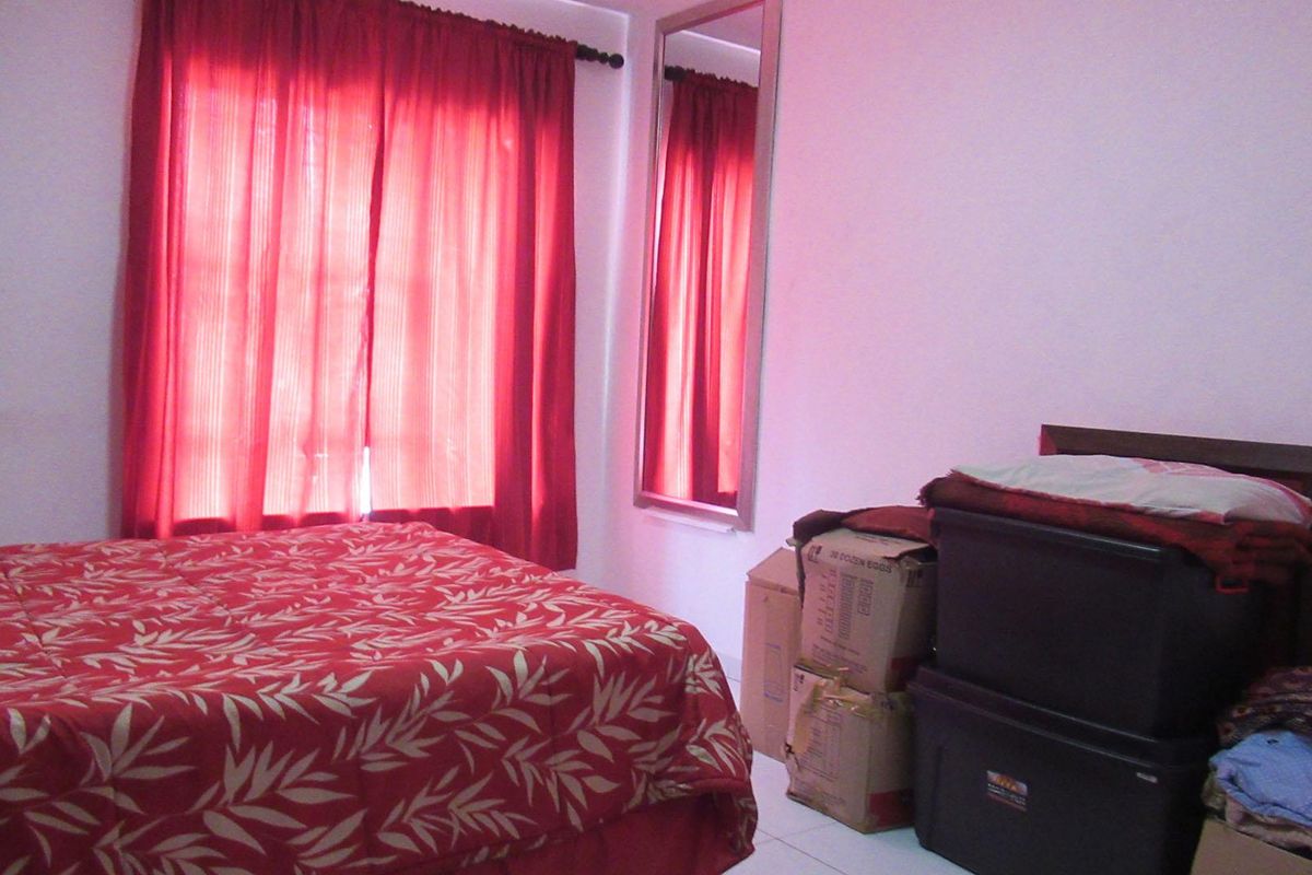 A bedroom featuring a wall-mounted mirror and window with red curtains, providing a functional space for rest.