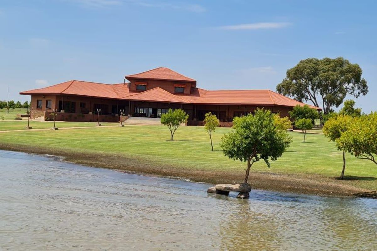 A spacious farm estate featuring a large residence with a terracotta tiled roof, set on expansive manicured lawns overlooking a private dam.