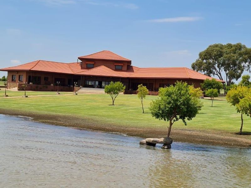 A spacious farm estate featuring a large residence with a terracotta tiled roof, set on expansive manicured lawns overlooking a private dam.