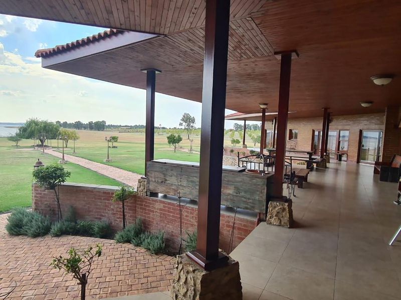 Spacious covered patio featuring brick and timber finishes, overlooking expansive farm grounds and a scenic waterfront view.