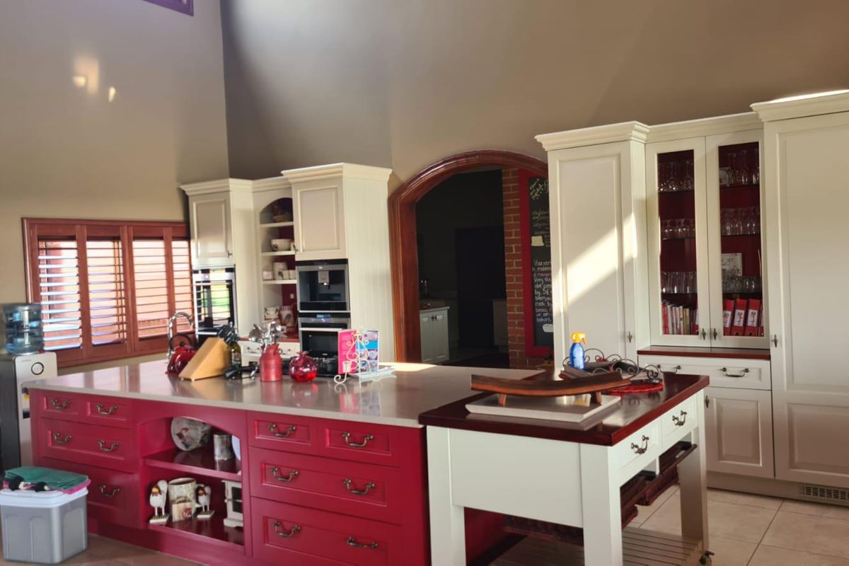 Spacious kitchen featuring a large central island with red cabinetry, integrated wall ovens, and custom cream-colored built-in cabinetry with glass-front display units.