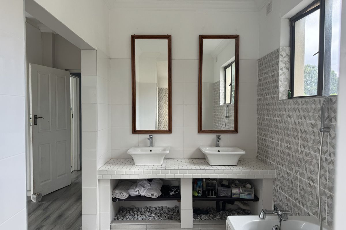A bright bathroom featuring a double vanity with vessel sinks, tiled countertop, wall-mounted mirrors, and a bathtub with a handheld shower attachment.