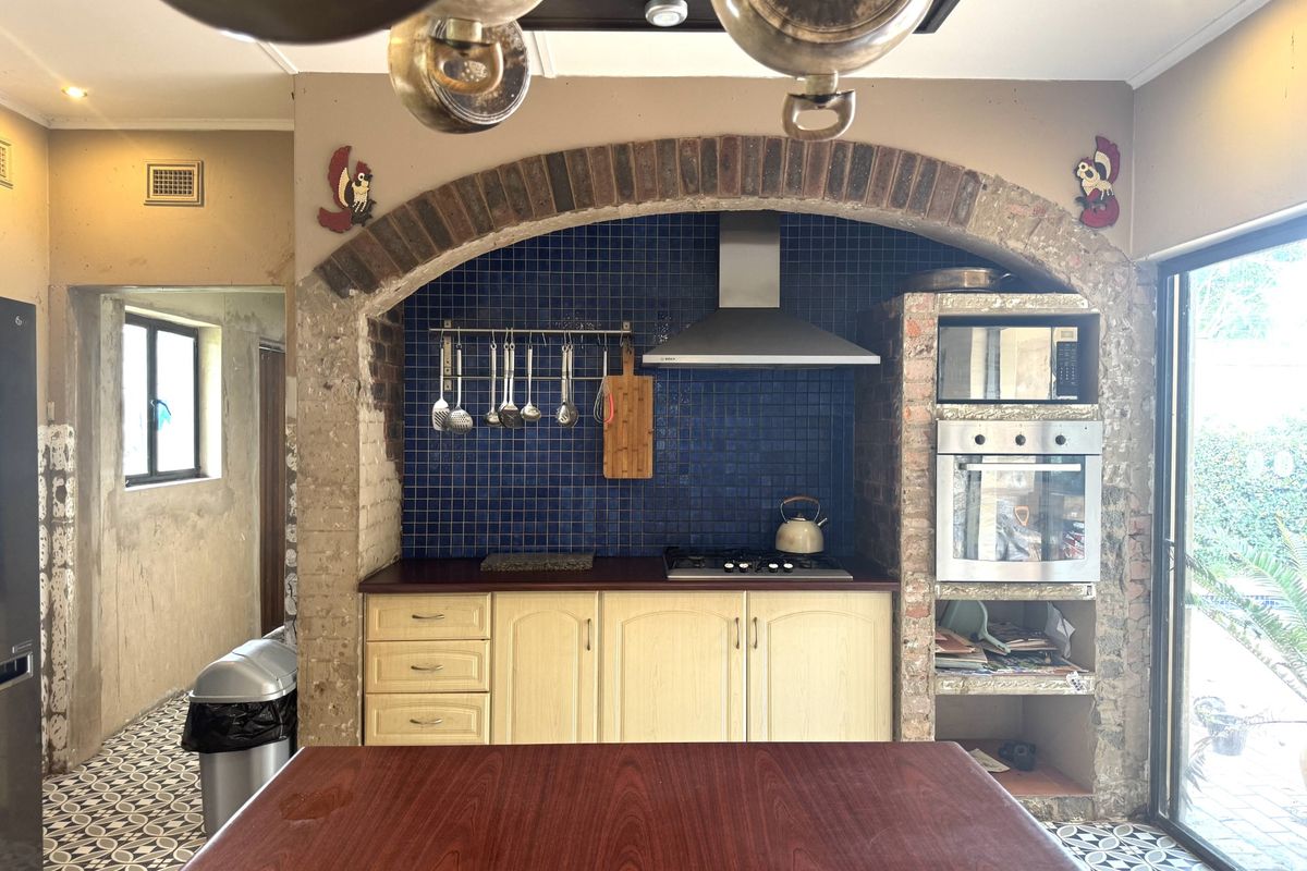 Kitchen featuring a rustic brick archway, blue mosaic backsplash, built-in oven, gas hob, and patterned floor tiles, offering a unique character-filled cooking space.