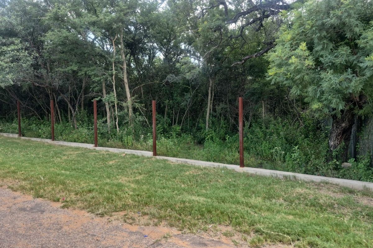 A view of the property boundary featuring a concrete plinth and installed metal fence posts bordering a wooded area.