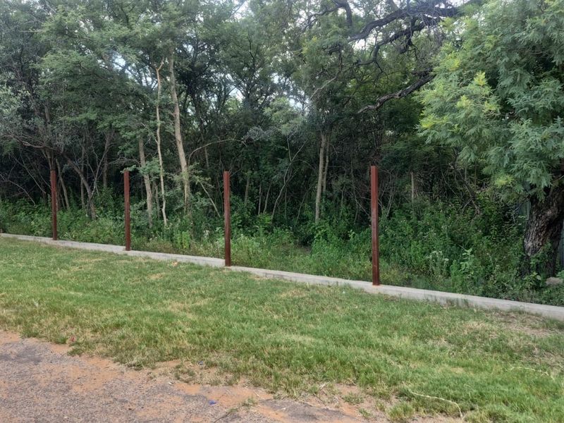 A view of the property boundary featuring a concrete plinth and installed metal fence posts bordering a wooded area.