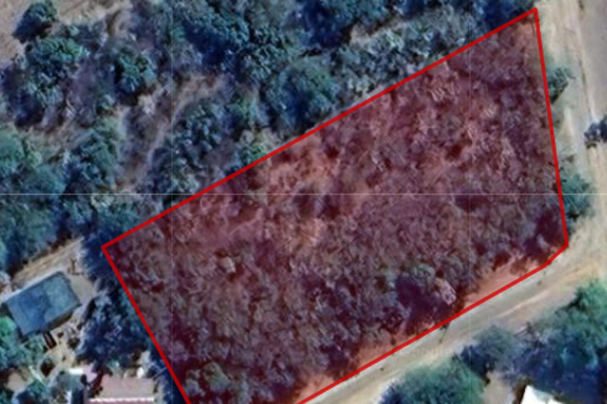 An aerial view of a vacant residential plot outlined in red, featuring natural vegetation and surrounding landscape.