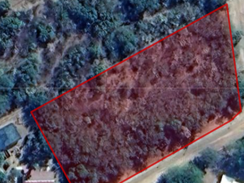 An aerial view of a vacant residential plot outlined in red, featuring natural vegetation and surrounding landscape.