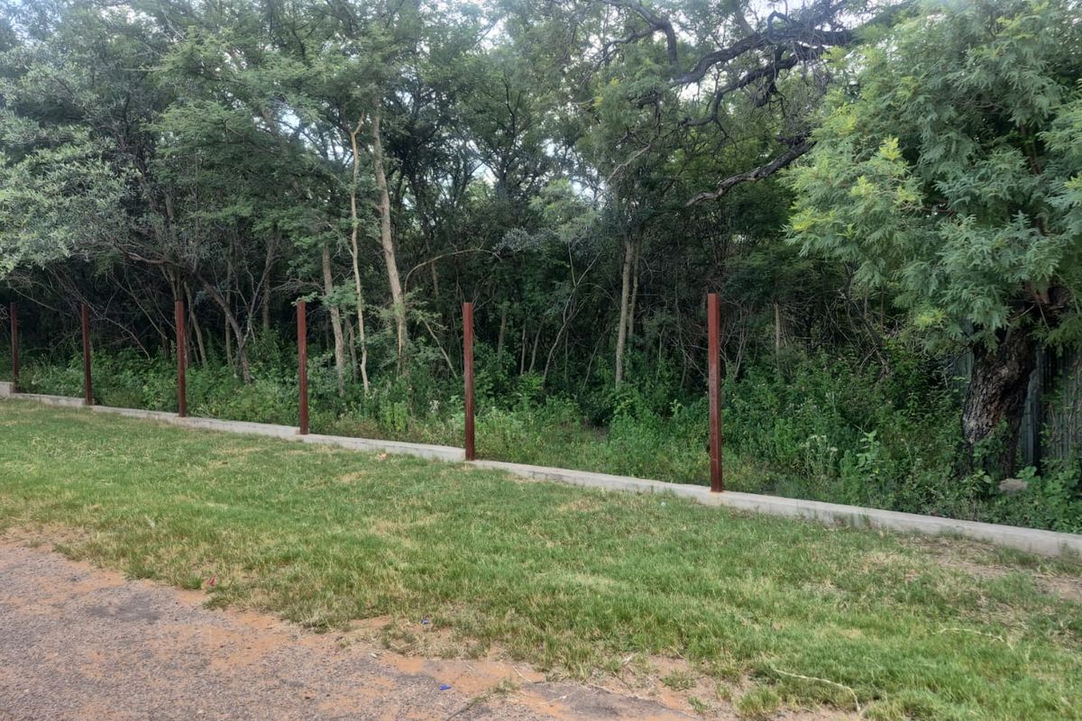 A view of the residential land boundary featuring a concrete retaining wall and installed metal fence posts against a backdrop of mature trees.