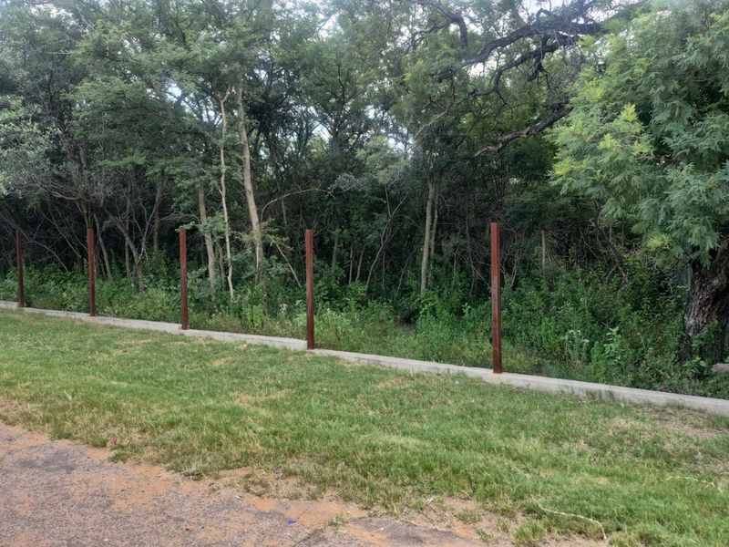 A view of the residential land boundary featuring a concrete retaining wall and installed metal fence posts against a backdrop of mature trees.