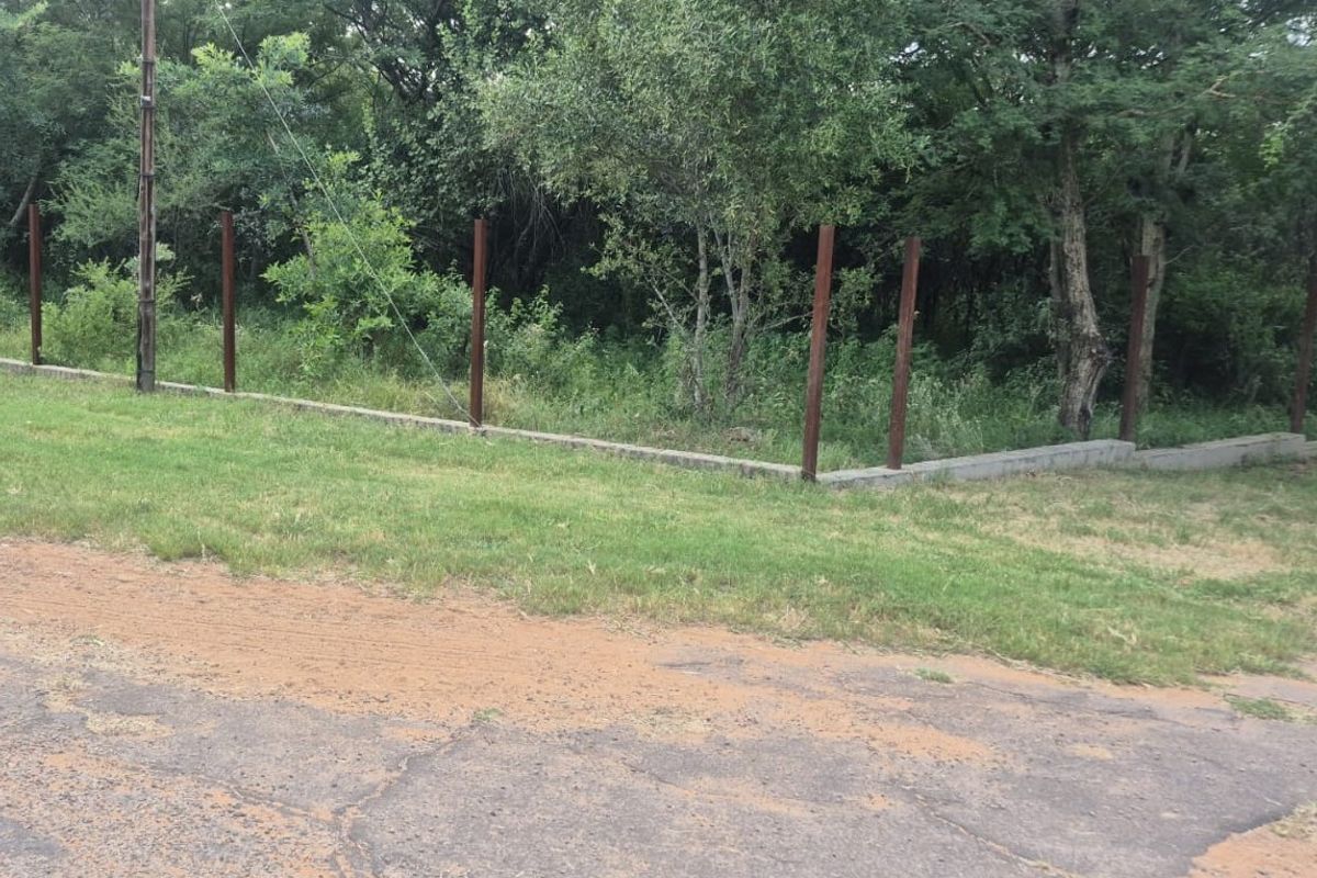 A vacant residential plot featuring a concrete boundary wall base and partially installed metal fence posts along the street frontage.
