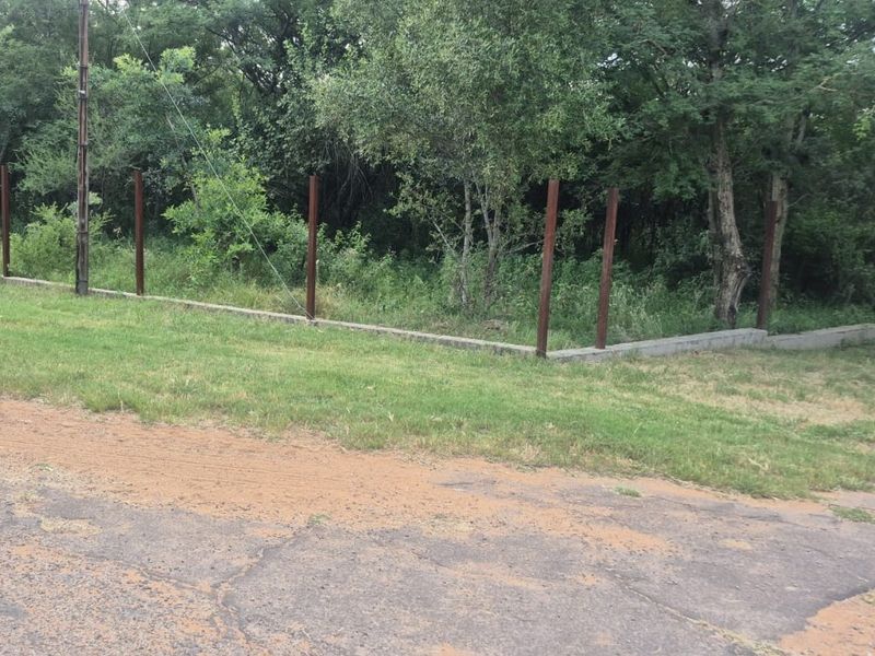 A vacant residential plot featuring a concrete boundary wall base and partially installed metal fence posts along the street frontage.