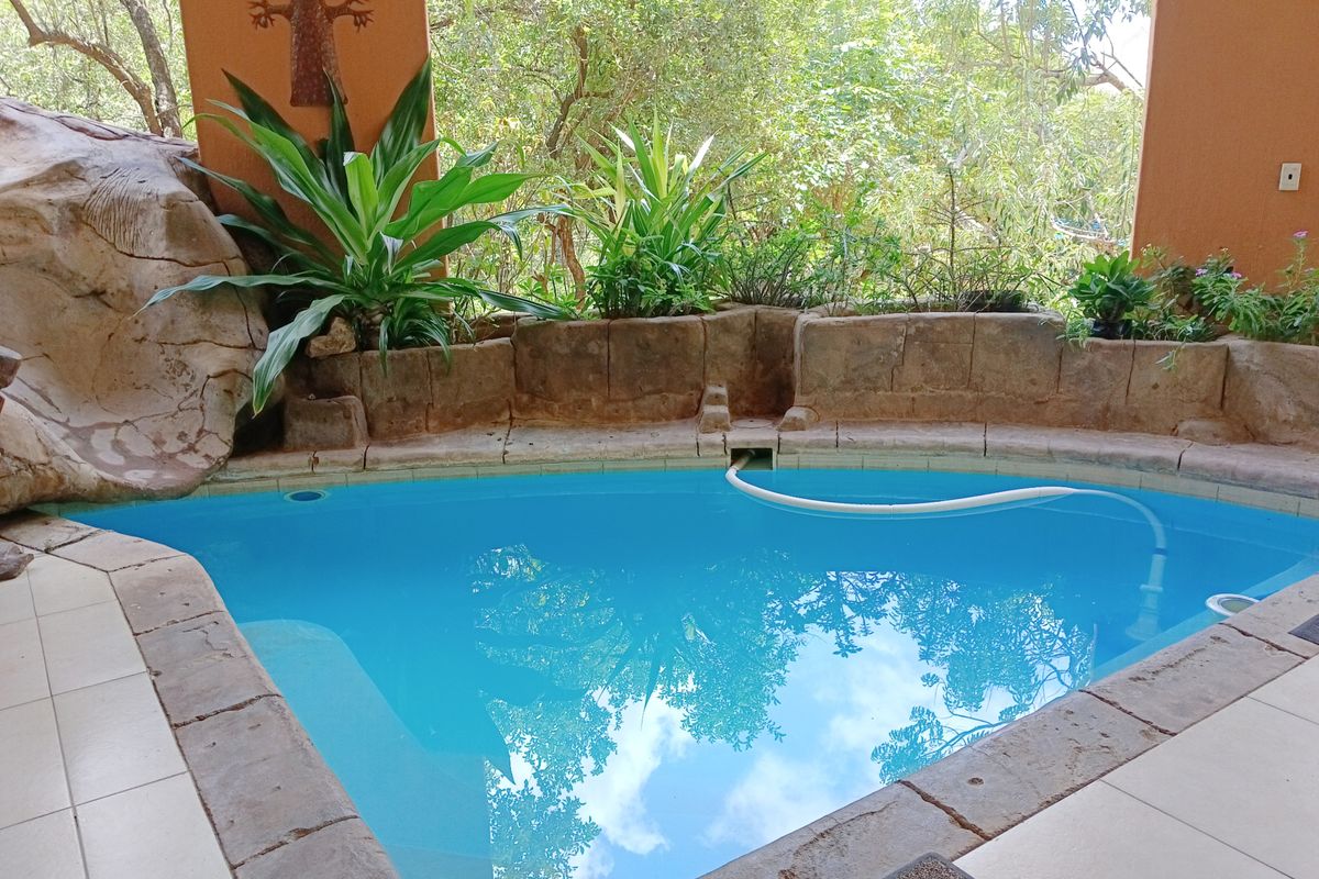 A private swimming pool area featuring built-in stone planters and a tiled surround, set within a covered patio space overlooking lush greenery.