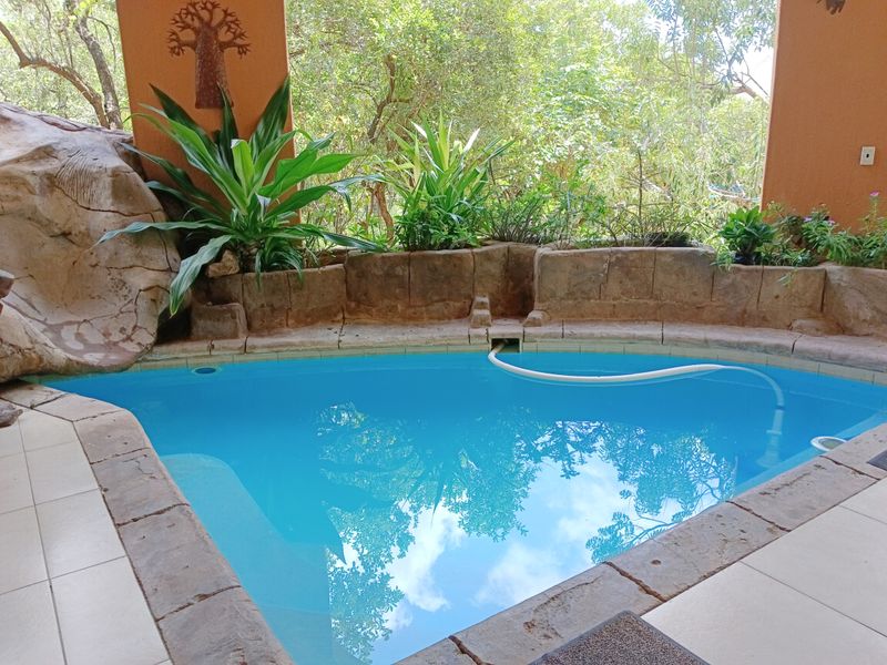 A private swimming pool area featuring built-in stone planters and a tiled surround, set within a covered patio space overlooking lush greenery.