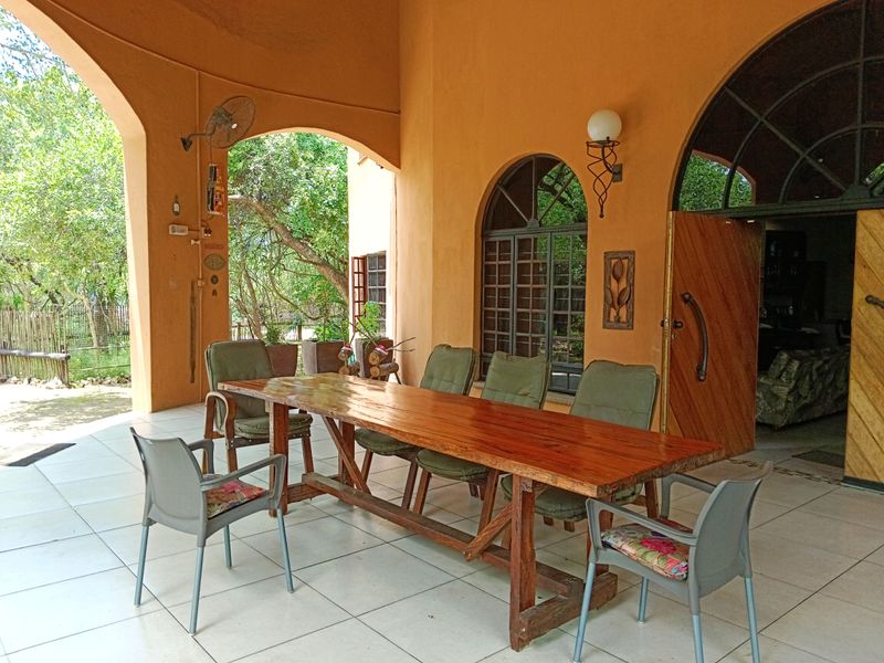 A spacious covered patio featuring tiled flooring, arched architectural details, and direct access to the garden area.
