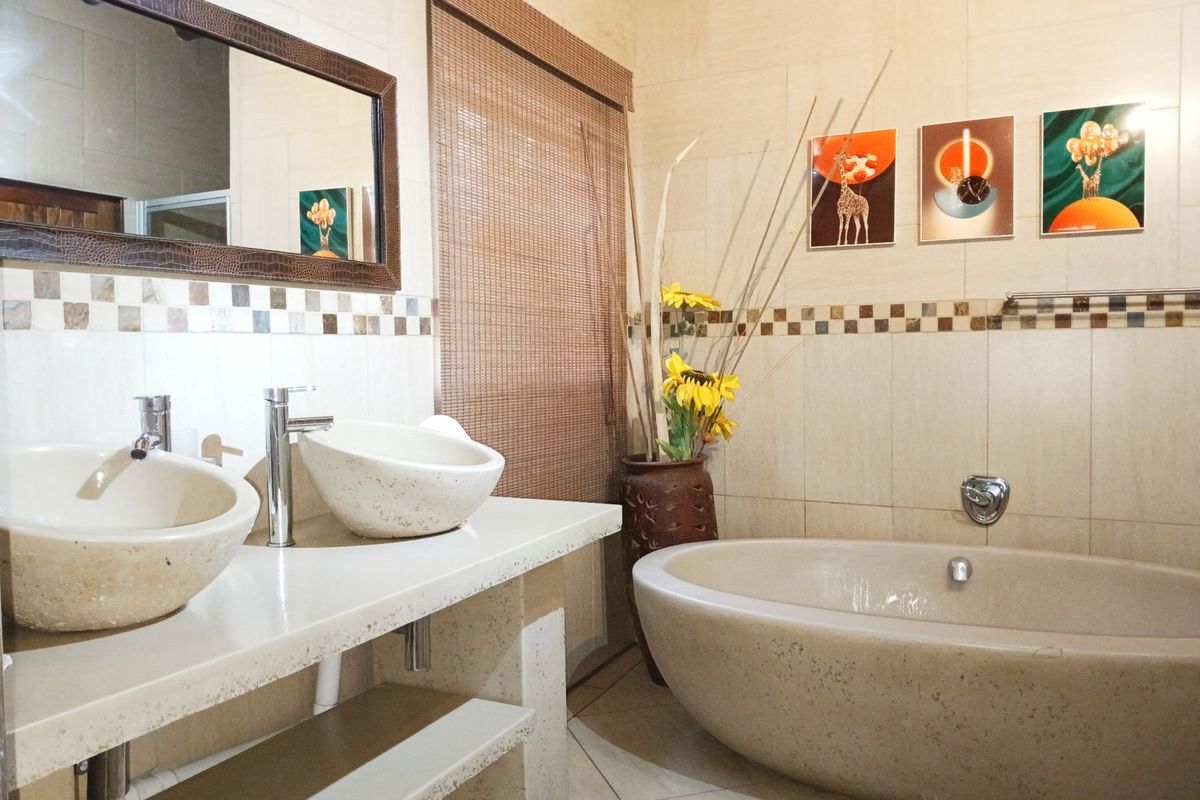 A well-appointed bathroom featuring a double vanity with stone vessel sinks, a modern freestanding stone bathtub, and elegant mosaic tile accents.
