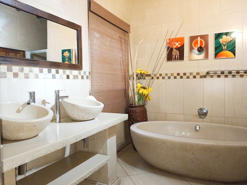 A well-appointed bathroom featuring a double vanity with stone vessel sinks, a modern freestanding stone bathtub, and elegant mosaic tile accents.