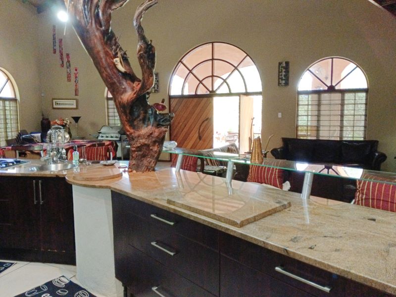 Spacious open-plan living and kitchen area featuring dark wood cabinetry, granite countertops, vaulted ceilings, and large arched windows providing natural light.