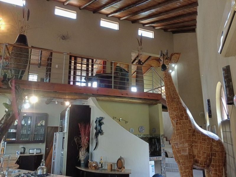 Spacious open-plan living area featuring a mezzanine level, exposed timber beam ceilings, and a functional kitchen with built-in cabinetry.