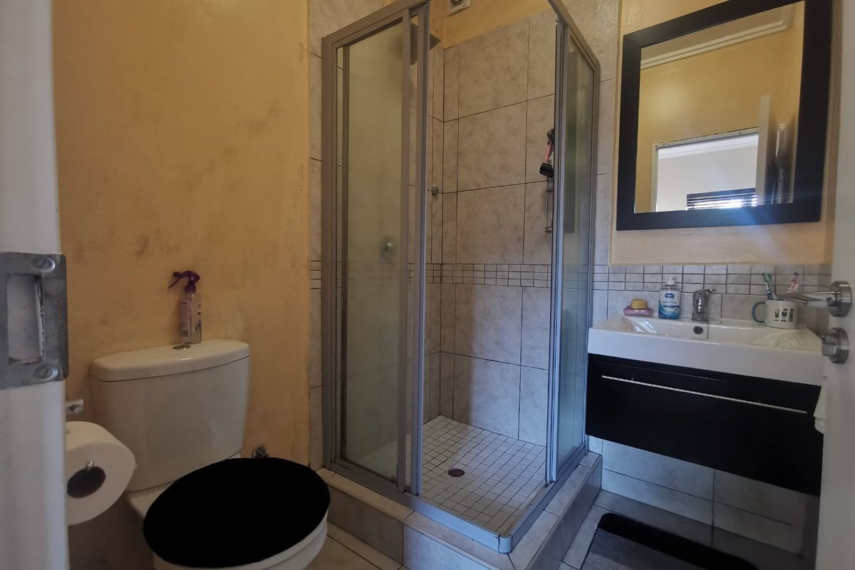 A functional bathroom featuring a glass-enclosed shower, a wall-mounted vanity with basin, and a standard toilet.