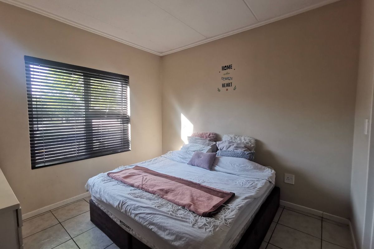 A functional bedroom featuring tiled flooring, a large window with fitted blinds, and neutral wall finishes.