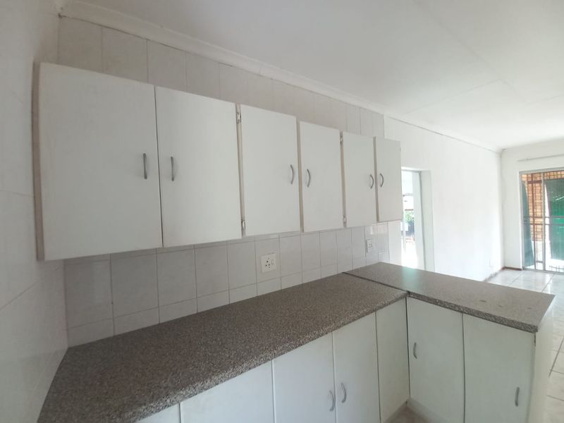 A functional kitchen area featuring white built-in cabinetry, laminate countertops, and tiled backsplash, offering a clean and neutral space ready for personalization.