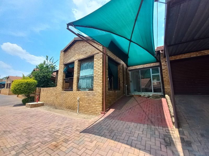 Front exterior view of the apartment featuring a face brick facade, paved driveway, carport, and a shade sail over the entrance.