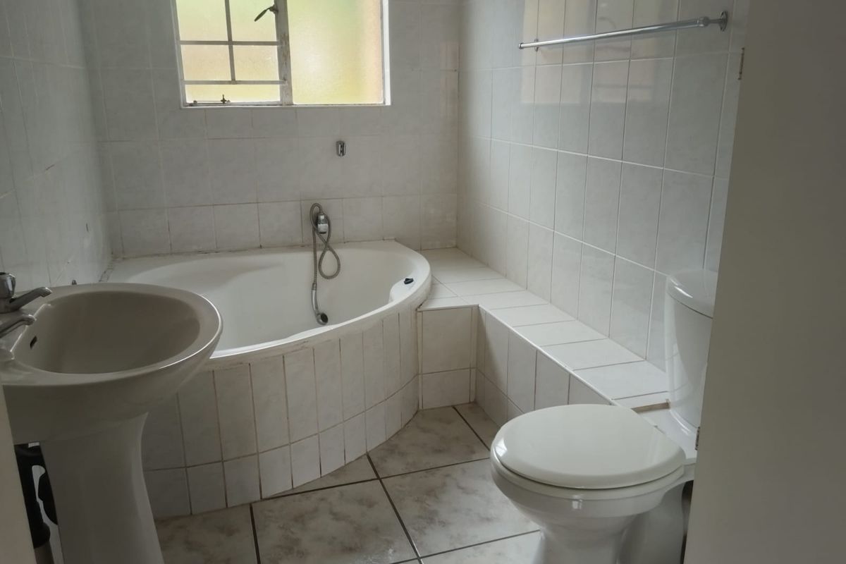 A functional bathroom featuring a built-in corner bathtub, pedestal basin, and toilet with white wall tiling and tiled flooring.