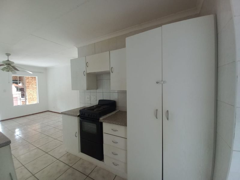 Open plan kitchen and living area featuring tiled flooring, white built-in cabinetry, and a freestanding stove, offering a functional and bright living space.