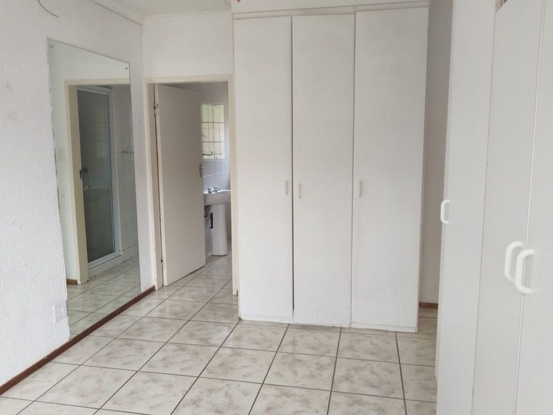 A bedroom featuring tiled flooring, built-in cupboards, and a large wall-mounted mirror, with an adjacent bathroom visible through the doorway.