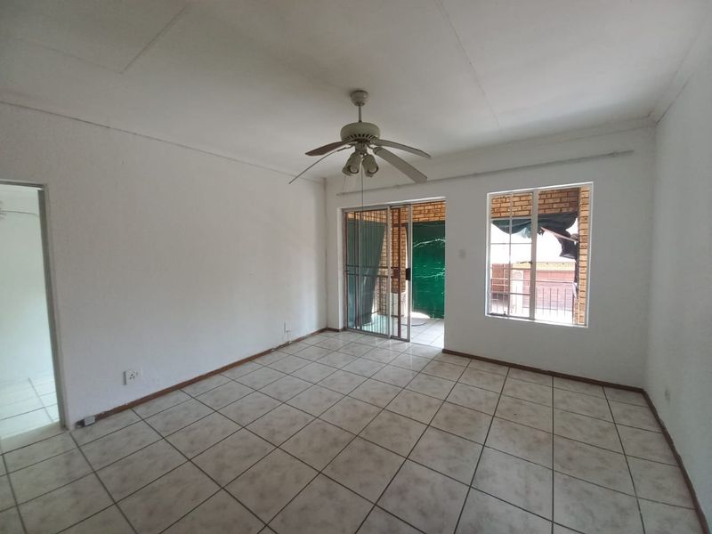 An empty living room featuring tiled flooring, a ceiling fan, and access to an outdoor area through a sliding glass door with security gate.