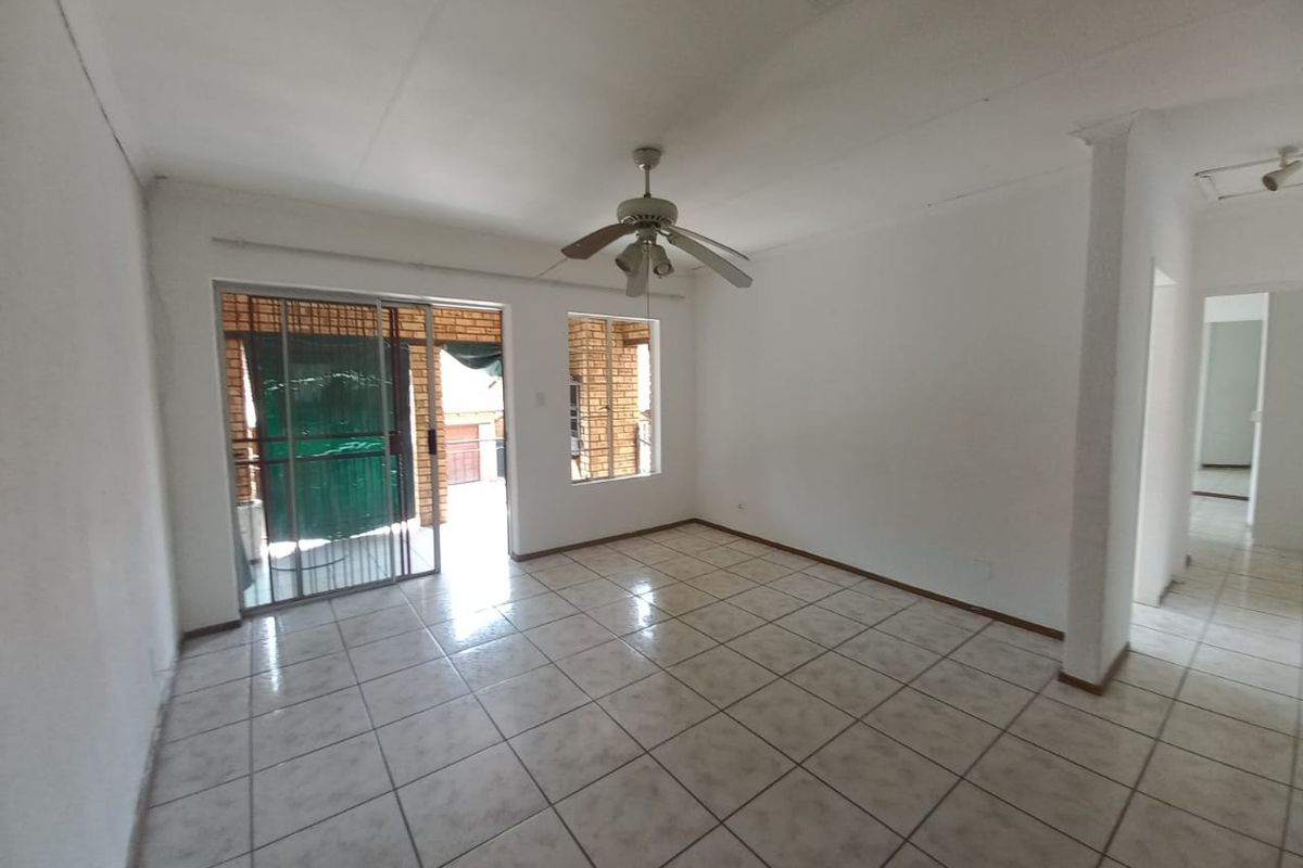 An empty living room featuring tiled flooring, a ceiling fan, and a sliding glass door leading to an outdoor area.
