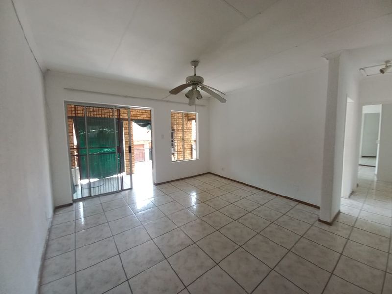 An empty living room featuring tiled flooring, a ceiling fan, and a sliding glass door leading to an outdoor area.
