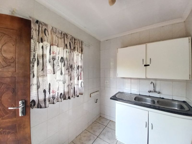 A compact kitchen featuring tiled walls, built-in cabinetry, and a double bowl stainless steel sink, offering a functional space ready for modernization.