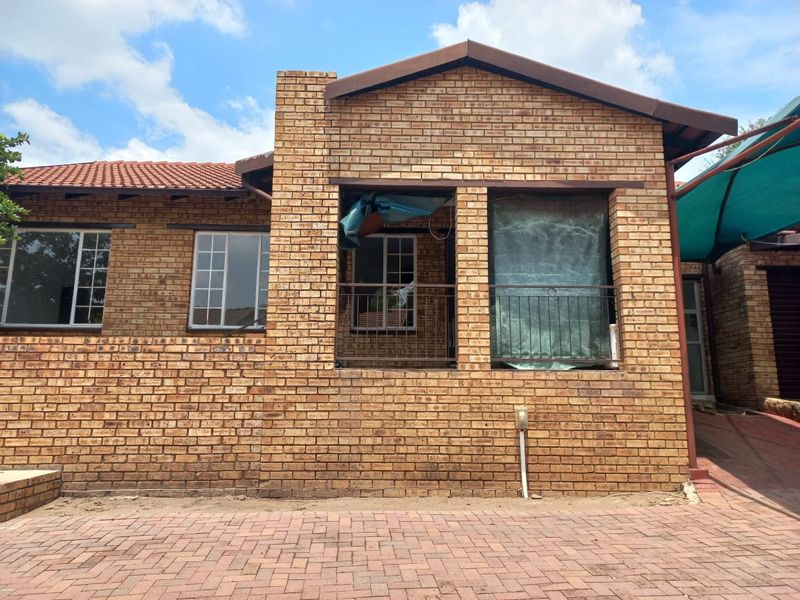 Front elevation of a face brick apartment building featuring a paved driveway, tiled roof, and a covered patio area with metal balustrades.