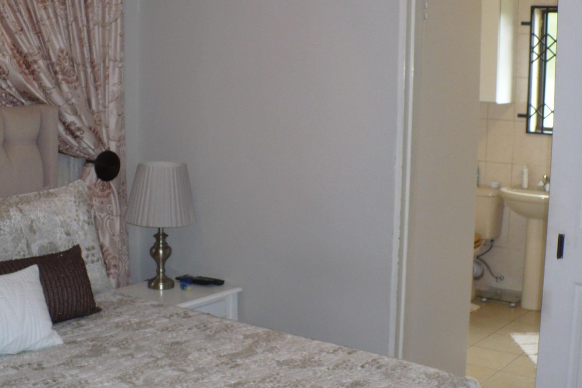 A bedroom featuring a neutral color palette with an adjoining en-suite bathroom visible through the doorway.