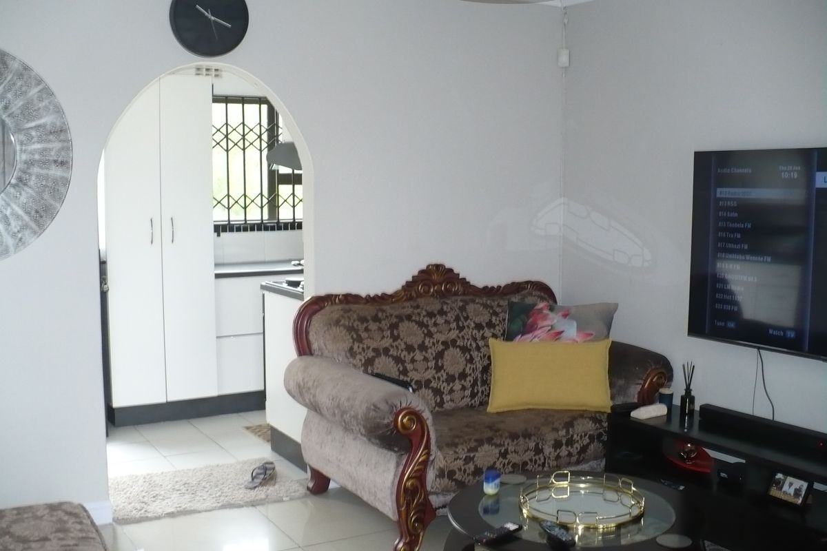 A living room featuring tiled flooring and an arched doorway leading to a kitchen area with built-in cabinetry.