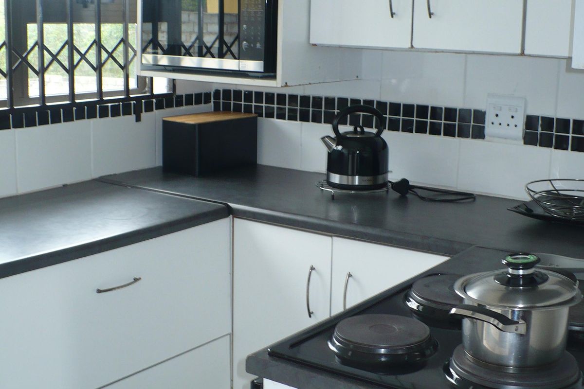 A functional kitchen featuring white cabinetry, dark countertops, a built-in microwave, and a black electric hob with an extractor fan.