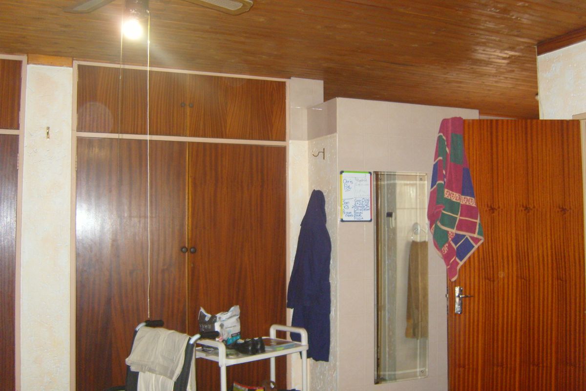 Bedroom featuring built-in wooden cupboards, a timber ceiling, and a ceiling fan. The room requires cosmetic updates to modernize the finishes.