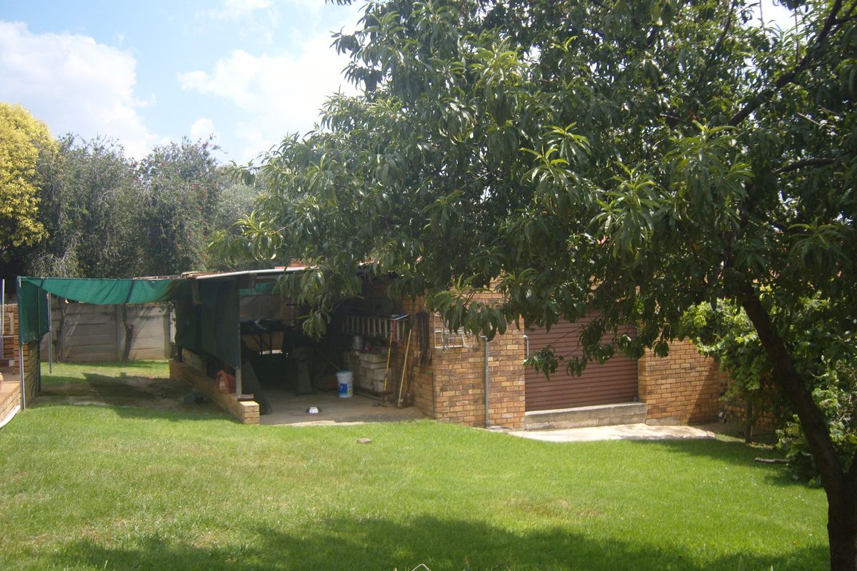 Rear garden view featuring a brick garage with a roller shutter door and an attached covered outdoor utility area.