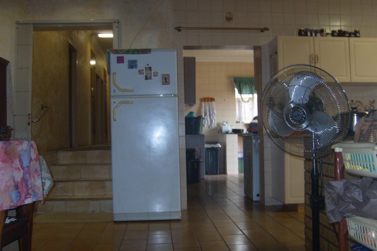 A dated kitchen area featuring tiled flooring and walls, with built-in cabinetry and a view through to an adjacent hallway and secondary prep area.