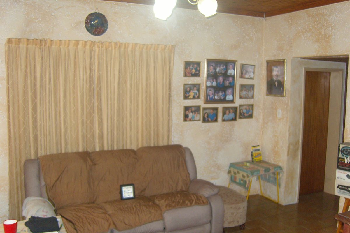 A living room featuring a timber ceiling, tiled flooring, and textured wall finishes, offering a dated aesthetic ready for modernization.