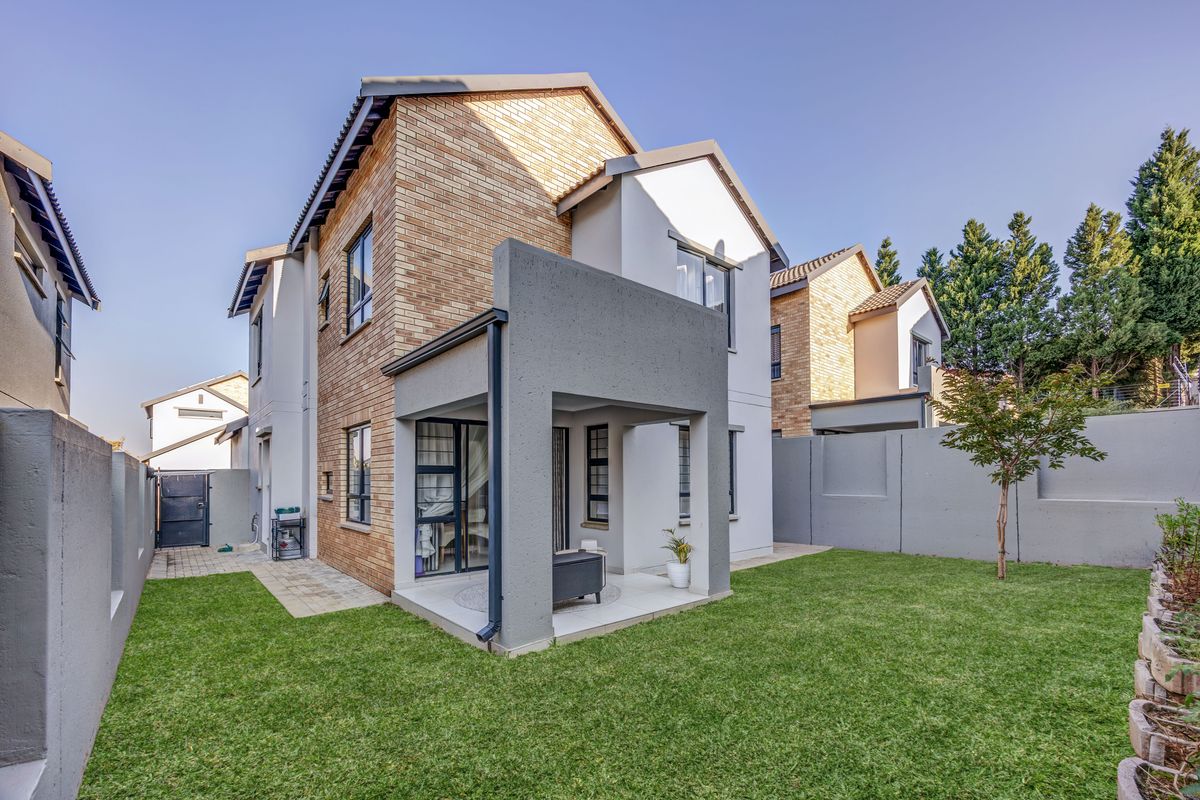Rear view of a double-story cluster home featuring a covered patio, brick and plaster facade, and a well-maintained private garden.